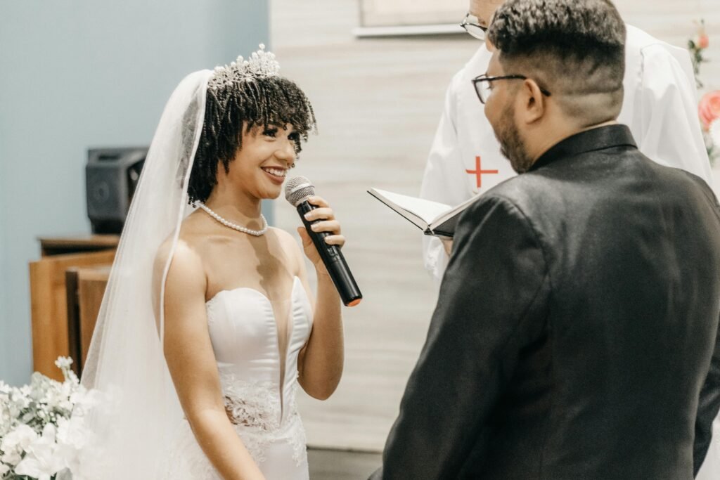 Bride joyfully speaking into microphone during indoor wedding ceremony, expressing love and commitment.