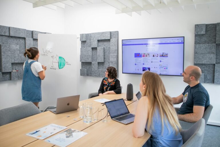 Team members engaging in a modern office meeting, discussing on a whiteboard and screen presentation.