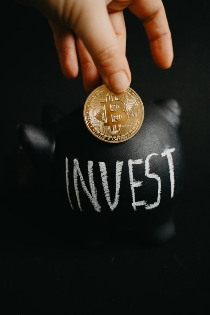 Gold bitcoin inserted into a black piggy bank labeled 'Invest', symbolizing cryptocurrency saving.