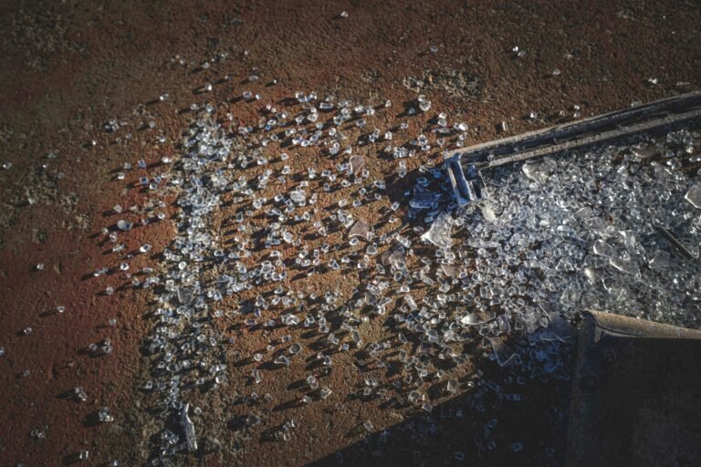 Close-up of shattered glass fragments scattered on a rough, textured surface in sunlight.